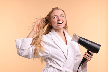 Wall Mural - Beautiful young woman drying her hair with hairdryer on beige background