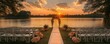 © peppastocker - Scenic outdoor wedding setup at sunset by a serene lake with floral archway