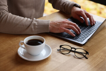 Man working on laptop at wooden table in cafe, closeup