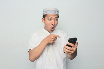 Asian Muslim man is playing with a smartphone with a white background.