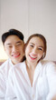 © ChayTee - Asia people young adult man woman relax smile look camera take photo post to social media vlog video at outdoor hotel balcony enjoy date day. Happy asian lover wife husband just married sweet newlywed