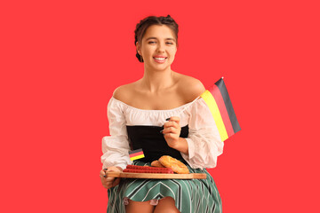 Wall Mural - Young Octoberfest waitress with German flag and traditional food on red background