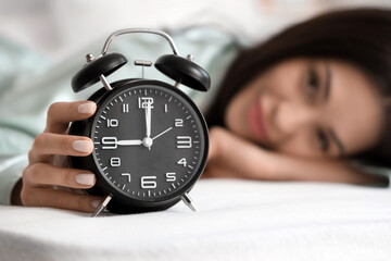 Wall Mural - Young woman with alarm clock lying in bedroom, closeup