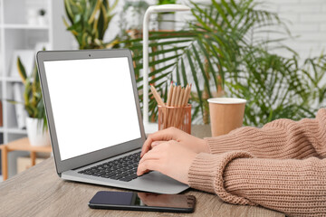 Wall Mural - Woman with modern laptop, mobile phone and color pencils working at wooden table in room