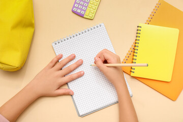 Wall Mural - Child's hands writing down something in notebook on beige background. Top view