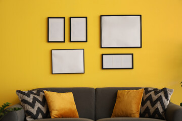 Wall Mural - Comfortable sofa and blank photo frames on yellow wall in room. Closeup