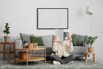 Wall Mural - Young woman with magazine sitting on floor in living room