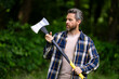 © Volodymyr - Lumberjack brutal bearded man in checkered shirt with ax on green nature. Man with axe in forest. Brutal woodsman. Lumberjack with an ax outdoor. The Lumberjack. Axe woodsman equipment.