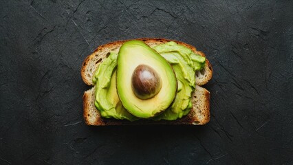 Wall Mural - Avocado spread elegantly laid on toasted brown bread with a halved avocado showcasing its rich green color and dark pit against a dark background.