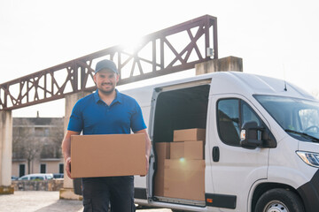 Fototapete - Smiling delivery driver handing over package in front of van. Delivery driver concept in a van. Man in blue uniform holding a package and smiling, representing a reliable delivery service.