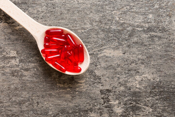 Wall Mural - Vitamin capsules in a spoon on a colored background. Pills served as a healthy meal. Red soft gel vitamin supplement capsules on spoon