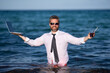 © Volodymyr - Fun business lifestyle. Freelance work, distance online work, e-working. Summer business. Business man in shirt remote working on laptop in sea water. Business man working online.
