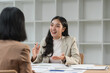 © crizzystudio - Two asian businesswomen engaging in a discussion about business strategy and investment planning while seated at their desks in a sleek, modern office environment