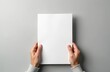 © Pete - Hands holding white blank paper sheet mockup isolated on gray background. Arm in shirt hold clear brochure template. Leaflet document surface simple print display.