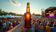 © Pete - Person holds cold beer bottle in hand at outdoor concert. Crowd cheers music event at summer festival, drinks. Refreshment in sunlight. Party, holiday mood, success.