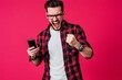 © schmidt - I am a winner, a happy man holding a smartphone and celebrating my success in front of a pink background