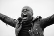 © schmidt - An African American male is captured from below in a black and white picture, ecstatically shouting and celebrating an achievement with his fists up while looking away