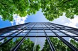 © AI Photo Stock - Green Building Skyscraper - Modern glass skyscraper reflecting lush green trees against a bright blue sky, symbolizing sustainable architecture and environmental consciousness