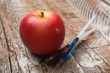 Wall Mural - GMO concept. Red apple and syringes on rustic wooden table, closeup