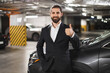 © sofiko14 - Young Caucasian male business professional in suit giving thumbs up gesture in parking garage. Concept of success, confidence, and approval.