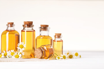 Wall Mural - Bottles of essential oil and chamomile flowers on white wooden table, closeup. Space for text