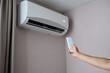 © GRON777 - Woman holding air conditioner remote control with display showing 20 degrees Celsius temperature in foreground against air conditioner on wall, sets comfortable cooling temperature on split system