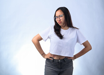 A young Asian woman with long dark hair and glasses, wearing a white crop top, stands with her hands on her hips and a skeptical expression against a plain white background.