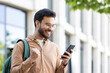 © Liubomir - Man outside university campus with phone in hand celebrating successful exam results, student with backpack holding hand up in triumph gesture, received online notification on smartphone.
