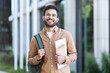 © Liubomir - Portrait of a happy successful student with books and backpack outside the university campus. The man is smiling and looking at the camera, dressed in casual clothes.