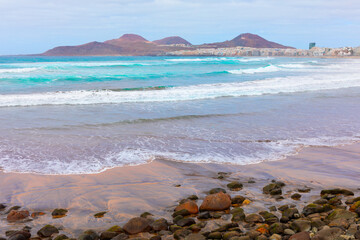 Wall Mural - Las Palmas de Gran Canaria, featuring Playa de Las Canteras with its golden sand, rocky shoreline, and waves. In background hills and the cityscape along the coast. A beautiful seaside view