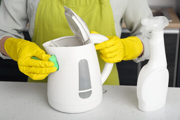 Wall Mural - Woman in yellow gloves cleaning electric kettle on white table