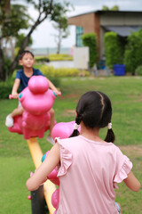 Asian child playing on toy seesaw toy in garden. Focus at the back of girl.