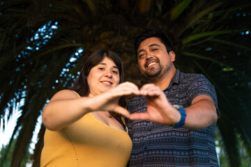 A man and a woman joyfully create a heart shape using their hands