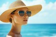 © HO - A high-fashion summer editorial image capturing a woman in sunglasses and a sun hat, exuding effortless elegance by the ocean.