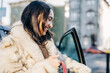 © Cavan Images - Smiling woman in fur coat opens car door on city street