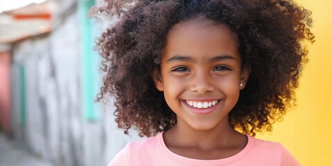 Wall Mural - A young girl with curly hair is smiling and looking at the camera. She is wearing a pink shirt