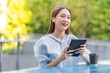 © StockPhotoRepublic - Beautiful Asian Woman Wearing Earbuds Using Tablet Outdoors a Greenery Office Building