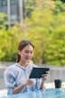 © StockPhotoRepublic - Beautiful Asian Woman Wearing Earbuds Using Tablet Outdoors a Greenery Office Building