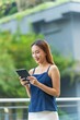 © StockPhotoRepublic - Young Asian Businesswoman In Casual Business Outfit Using Tablet Outdoors In Front a Modern Office Building