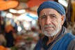 © c80 - Elderly man with a blue headscarf looks directly at the camera in a busy market scene in mid-afternoon light