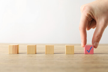 Woman taking pink cube with check mark at wooden table, closeup