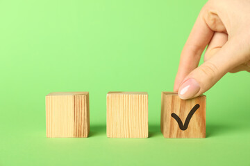 Wall Mural - Woman taking wooden cube with check mark on green background, closeup