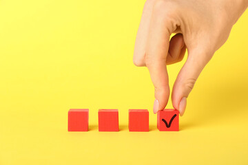 Wall Mural - Woman taking red cube with check mark on yellow background, closeup