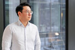 © RomArt production - Businessman wearing casual formal attire standing by office window with a thoughtful look. The modern glass background complements the scene, reflecting the mood of ambition and contemplation.