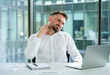 © RomArt production - Professional man in a modern office setting feeling neck discomfort while using a laptop. Dressed in business attire, conveying workplace challenges and ergonomic issues in a corporate environment.