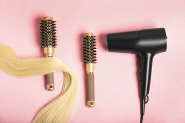 Wall Mural - Stylish round brushes, lock of blonde hair and hairdryer on pink background, flat lay