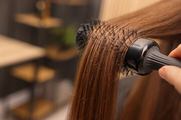 Wall Mural - Hairdresser styling client's hair with round brush in salon, closeup