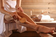 © New Africa - Woman massaging her leg with brush at sauna, closeup