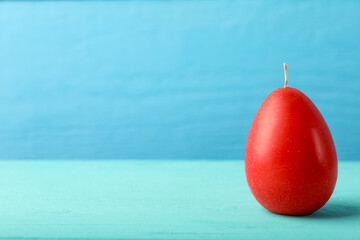 Wall Mural - Red egg-shaped candle on turquoise wooden table against light blue background, space for text. Easter decor