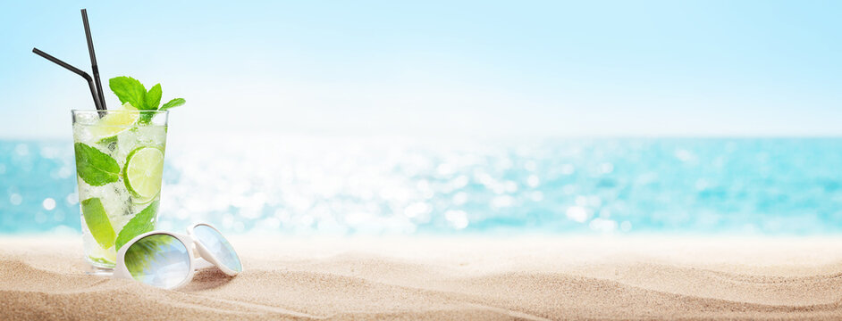 Fototapete -  - A refreshing mojito cocktail with fresh mint and lime, placed next to stylish sunglasses on beach